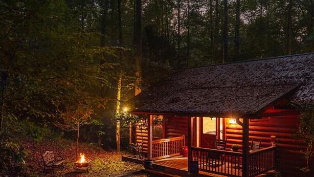 A cozy cabin with a porch, a fire pit, and a small table.