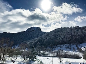 A snow-covered landscape with a mountain, trees, and a bench. - Hôtel Les Mouflons (Mont-Dore)