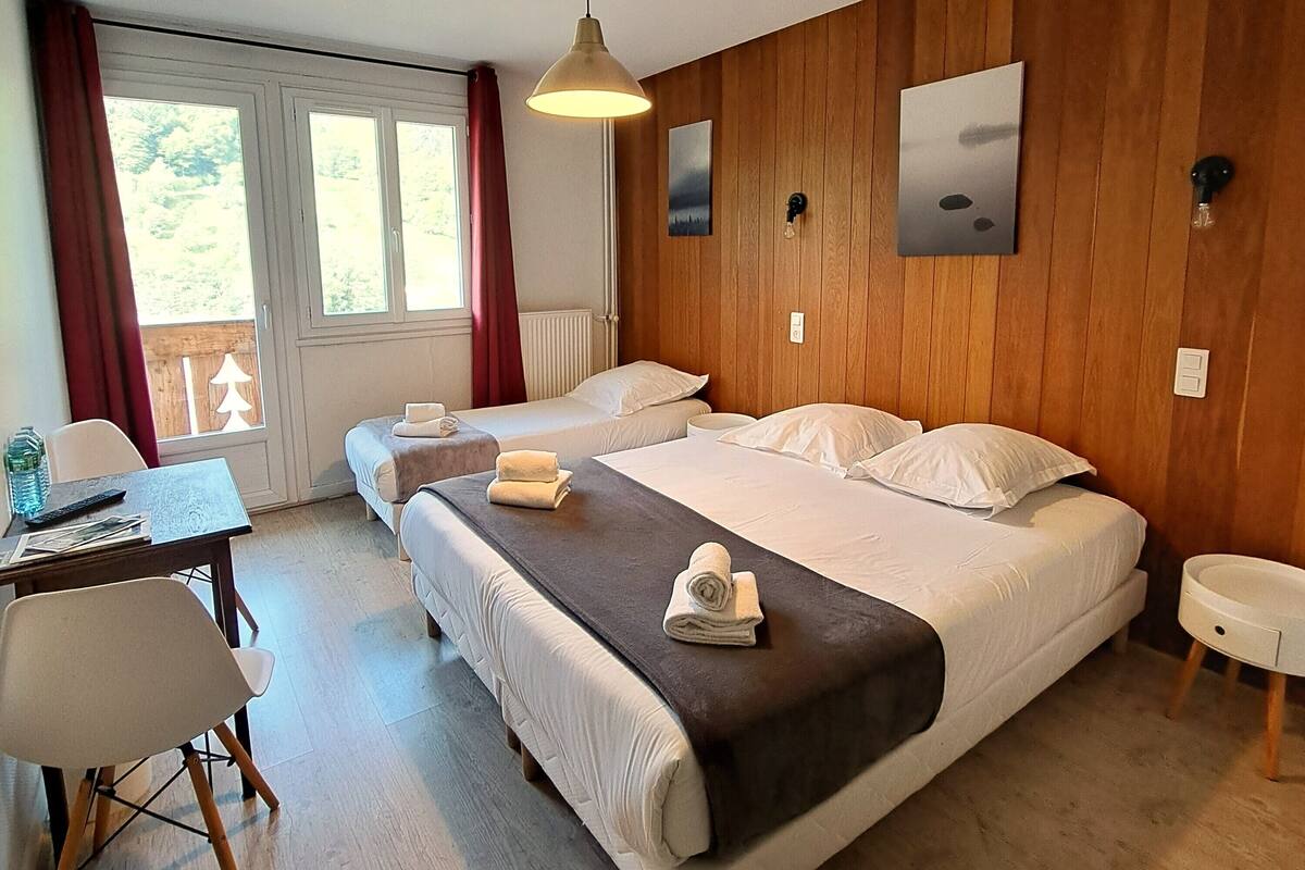 Une chambre d’hôtel avec deux lits, un bureau avec une chaise, une petite table et une fenêtre avec des rideaux.