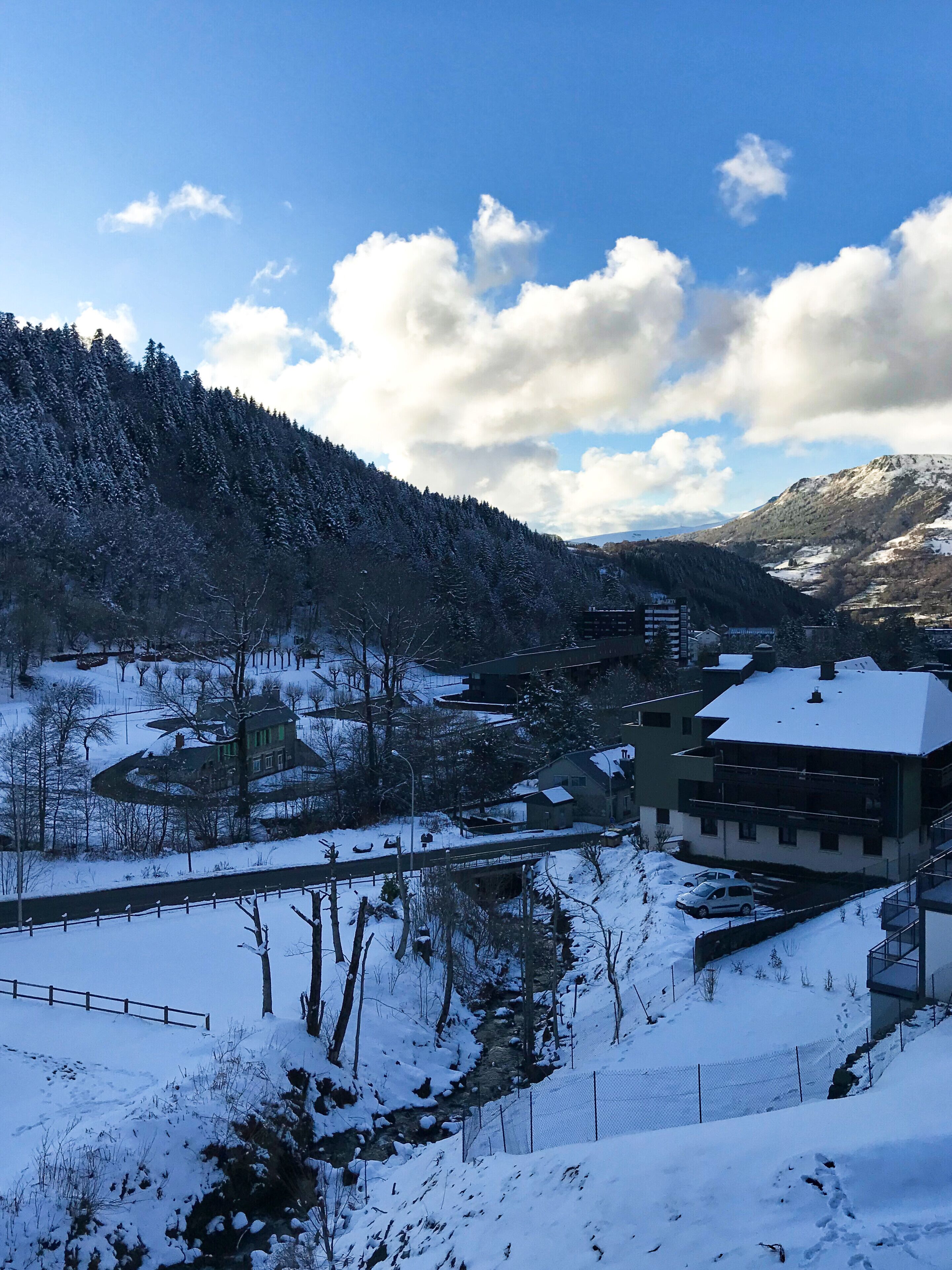 A snow-covered landscape with a river, buildings, and a forested mountain.