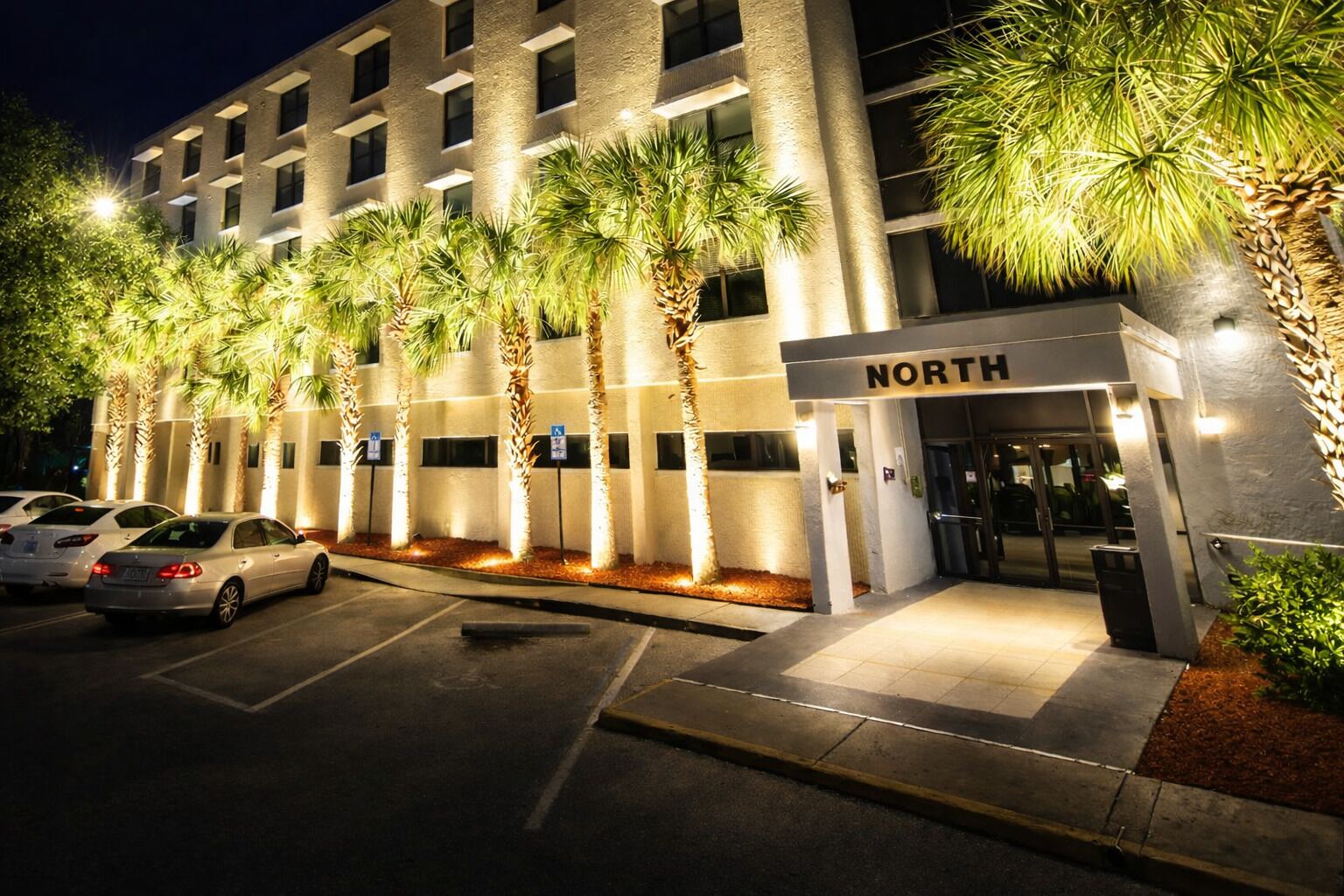 Een meerhoog hotel met een 'NORTH' bord, parkeerplaats en palmbomen.