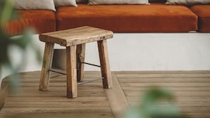 A wooden stool in a room with a wooden floor, a sofa with cushions, and a hanging light fixture. - Hoy Paris - Home of YOGA (Paris)