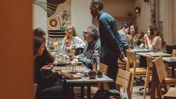 Un restaurante con techo alto y tragaluces, mesas y sillas de madera, y un ambiente informal para comer.