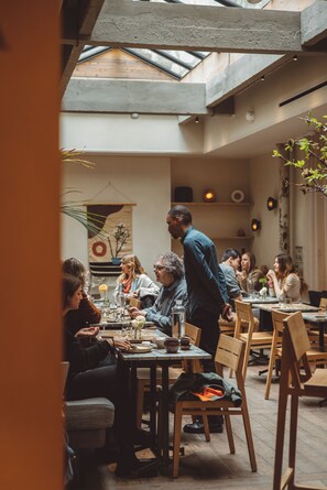 Un restaurante con techo alto y tragaluces, mesas y sillas de madera, y un ambiente informal para comer.
