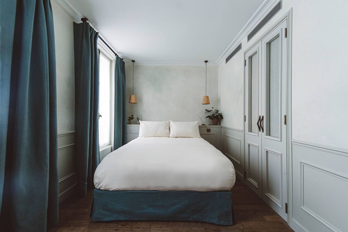Un dormitorio con una cama grande, una mesita de noche con lámpara y un aparador con espejo.