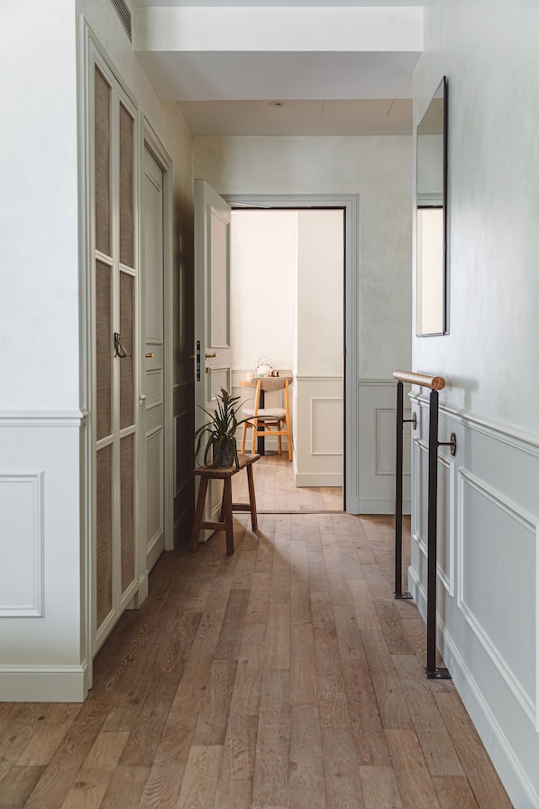 A hallway with wooden flooring, white walls, and a mirror on the right. There is a door leading to another room and a small table with a plant. - Hoy Paris - Home of YOGA (Paris)