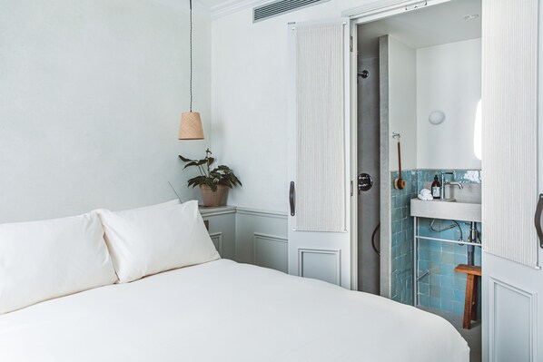 Un dormitorio con cama, planta en maceta, lámpara colgante y baño con lavabo y ducha.