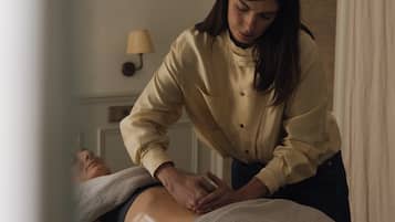 A person receiving a massage in a room with a window, a wall-mounted lamp, and a decorative wall piece.
