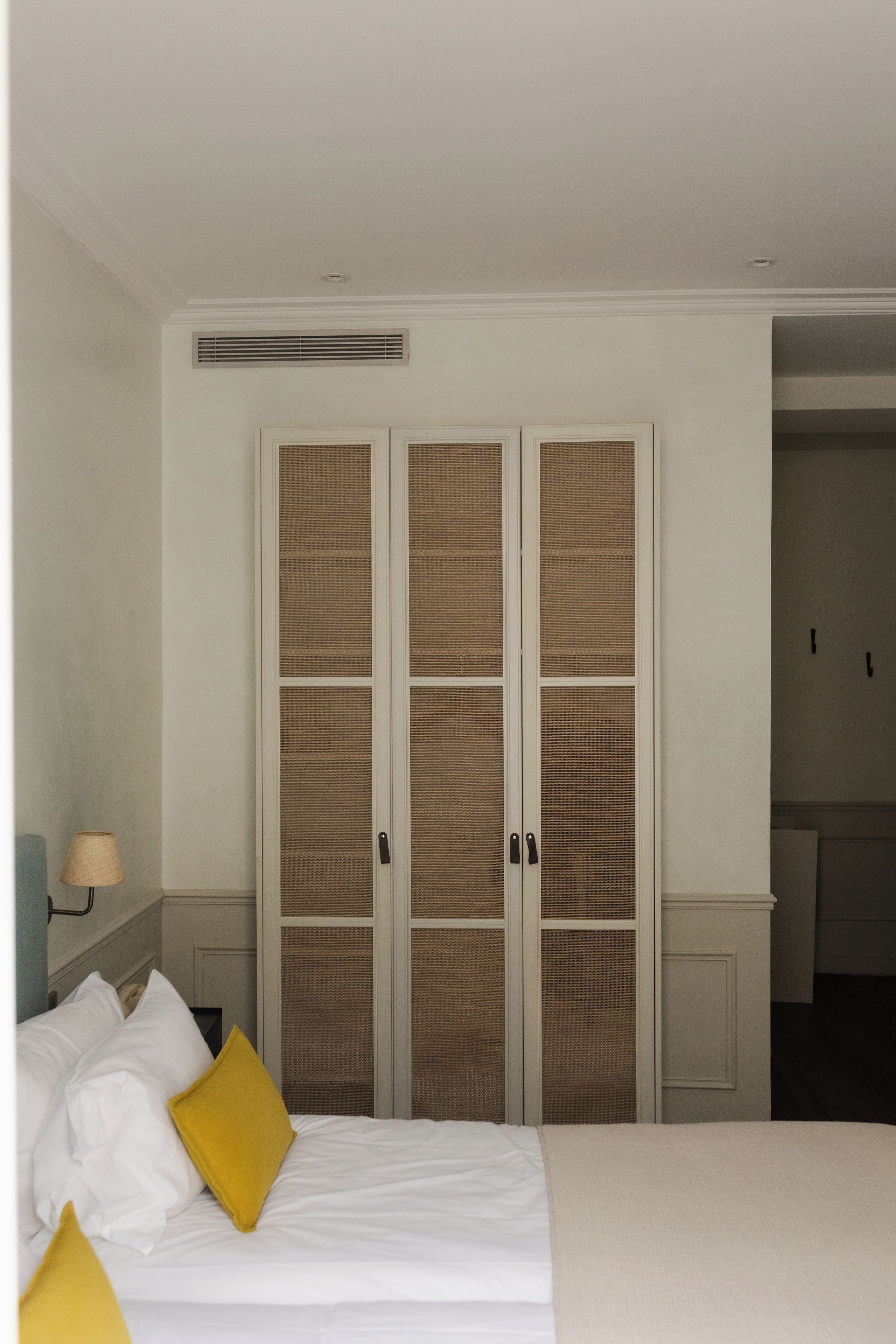 Una habitación de hotel con una cama, una mesita de noche, una lámpara y un armario con puerta de malla.