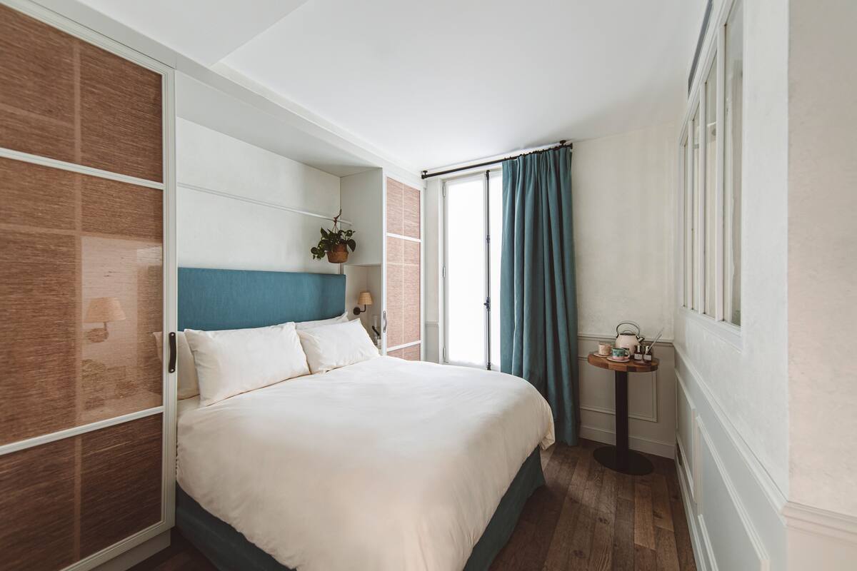 Un dormitorio con cama, mesita de noche, planta colgante y ventana con cortinas.
