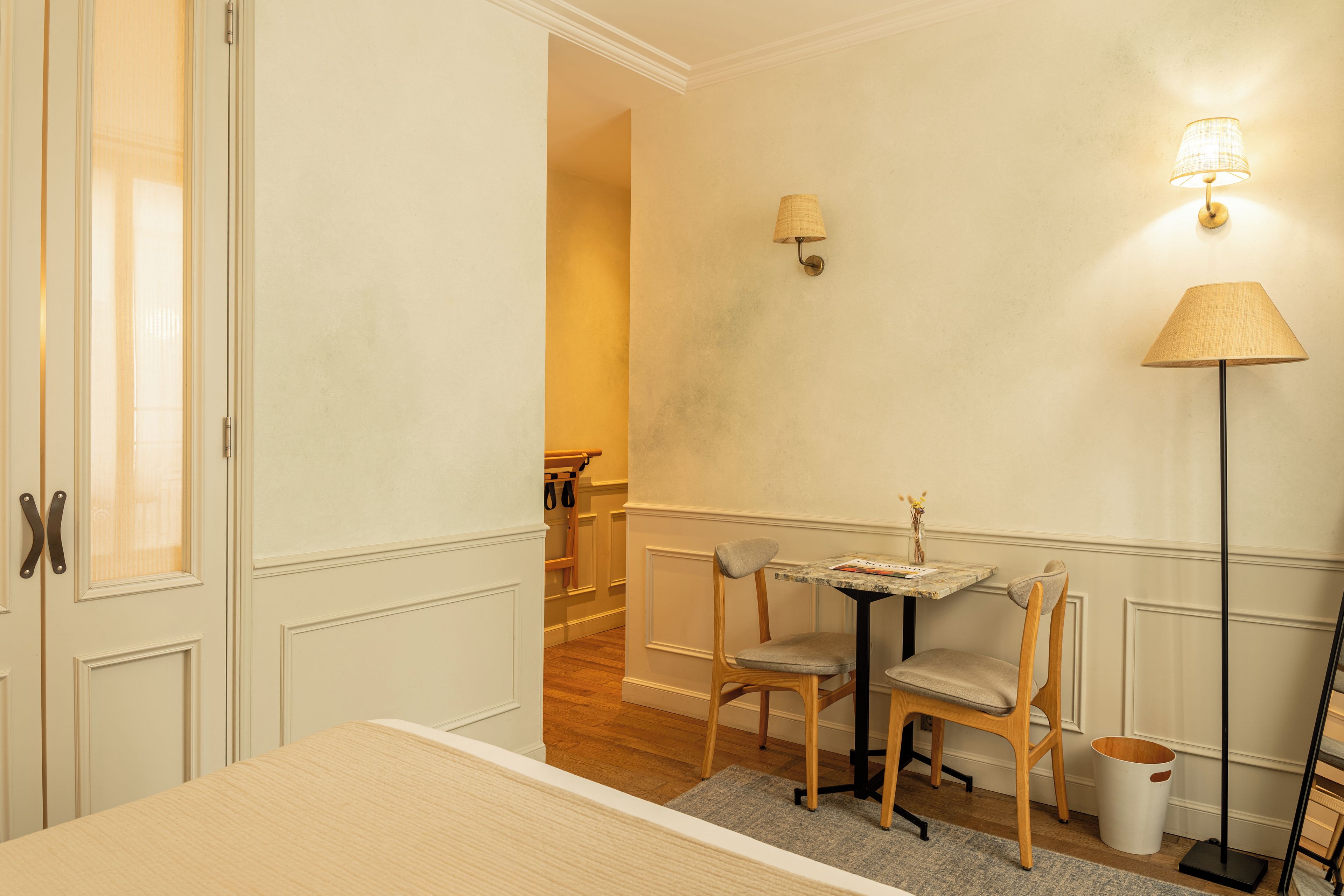 Ein Hotelzimmer mit Bett, einem kleinen Tisch mit Stühlen, einer Stehlampe und einer Wandleuchte.