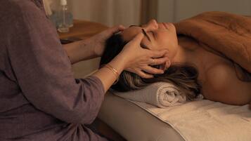 Une personne reçoit un massage dans une pièce où se trouve une table en bois et une bouteille d’eau posée sur une petite table d’appoint.