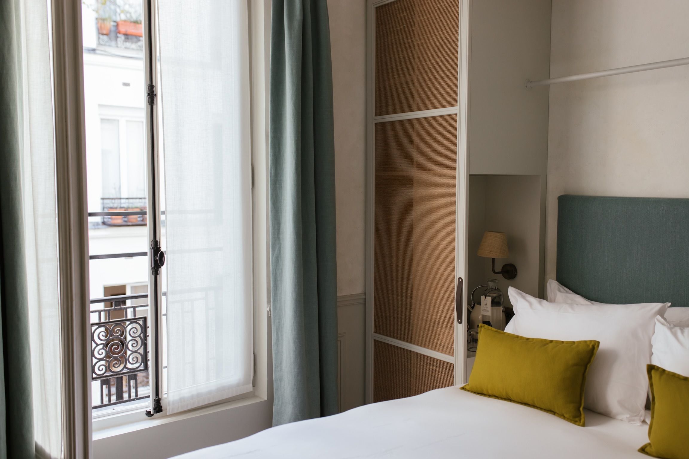 Quarto de hotel com cama, janela com cortinas, vista para a rua e luminária na parede.