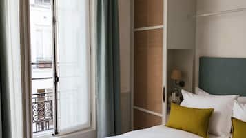 Quarto de hotel com cama, janela com cortinas, vista para a rua e luminária na parede.