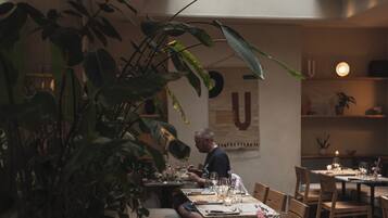 Un espacio interior comedor con mesas, sillas y una planta grande en maceta.