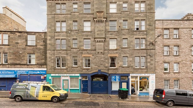 A multi-story building with a central entrance, several windows, and storefronts on the ground floor. - Silver Lining - St Leonard St Apartment (Edinburgh)