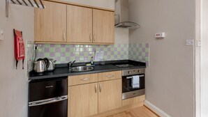 A compact kitchen with light wood cabinets, a stainless steel refrigerator, an oven, and a sink. - Silver Lining - St Leonard St Apartment (Edinburgh)