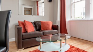A modern living room with a brown leather sofa, a glass coffee table, and a large mirror on the wall. - Silver Lining - St Leonard St Apartment (Edinburgh)