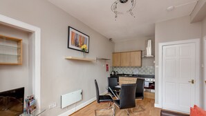 A modern living room with a TV, glass coffee table, and a red rug. A dining area with a table and chairs is visible in the background. - Silver Lining - St Leonard St Apartment (Edinburgh)