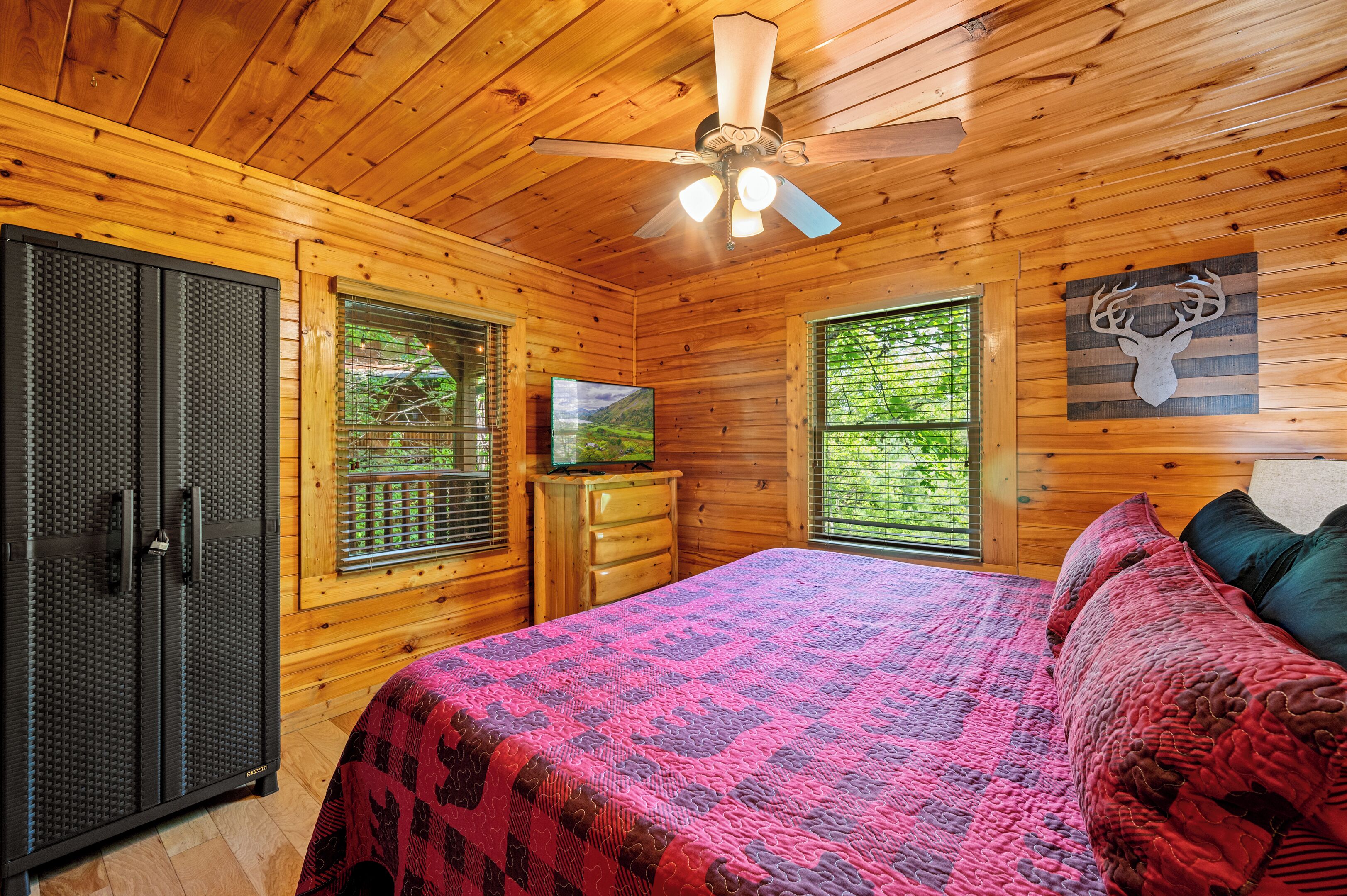 Ein Schlafzimmer einer Holzhütte mit Bett, Schminktisch, Fernseher und Deckenventilator.