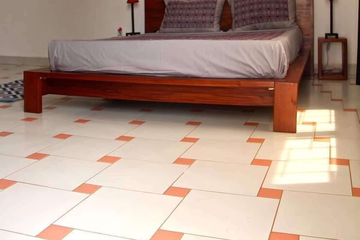 Ein Schlafzimmer mit einem hölzernen Bett, weiß-orange gefliestem Boden und je einer roten Lampe auf beiden Seiten des Bettes.
