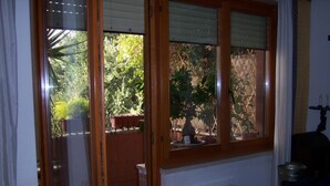 A room with a window overlooking a garden, a radiator, and a small table with a lamp. - Talenti house (Roma)