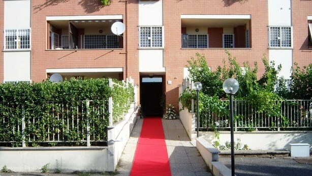 A multi-story apartment building with a red carpet leading to the entrance. - Talenti house (Roma)