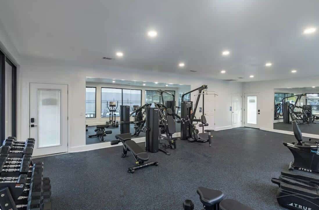 A gym with exercise equipment, large windows, and a mirrored wall.