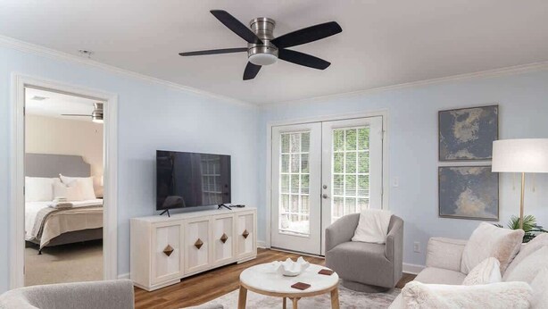 A living room with a ceiling fan, a television, a white cabinet, a gray armchair, a white sofa, and a round coffee table.
