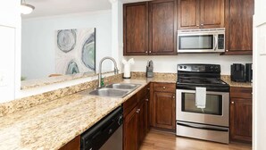 A kitchen with granite countertops, stainless steel appliances, wooden cabinets, and a painting on the wall.