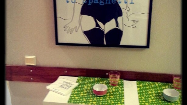 A framed artwork with a silhouette of a woman and text, a small table with a green checkered tablecloth, and a chair. - City Drops Hostel (Porto)