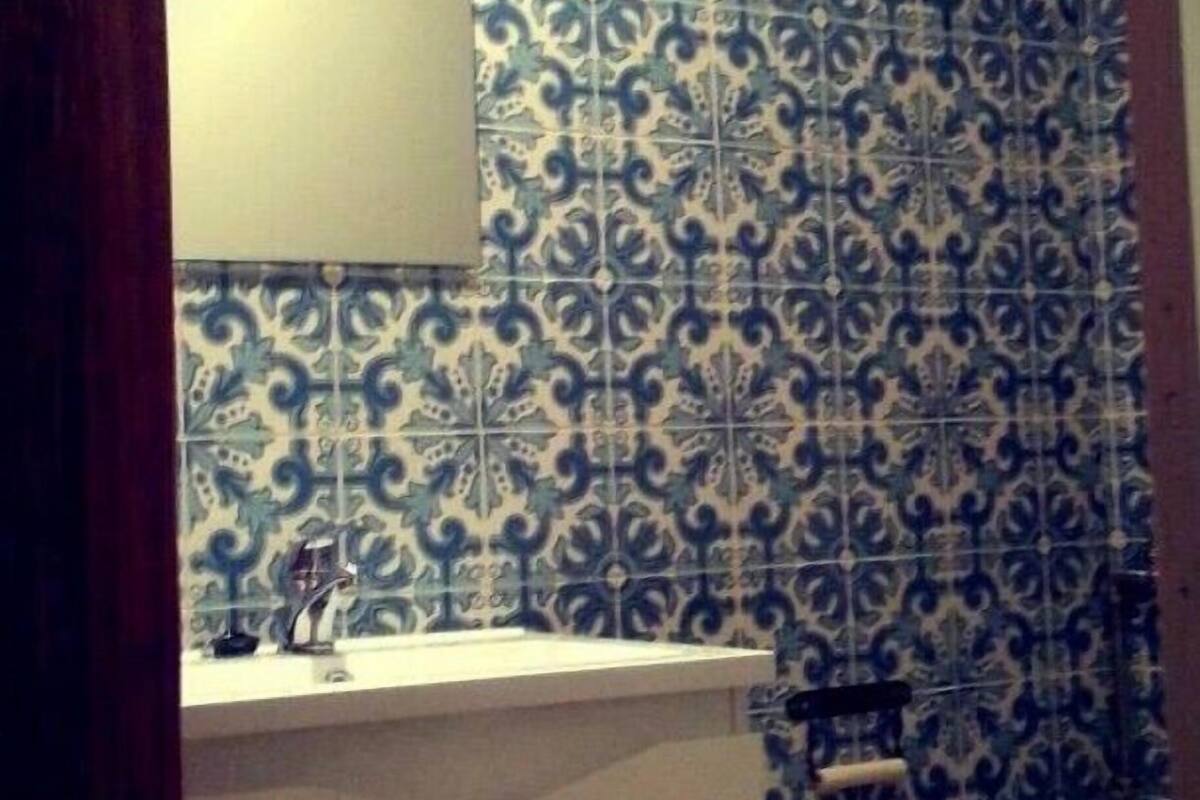 A bathroom with blue patterned tiles, a white sink, and a framed picture on the wall.