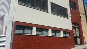 A modern two-story building with a white facade and red brick lower section, featuring large windows and a visible door. - City Drops Hostel (Porto)