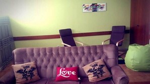 A purple tufted sofa with two decorative pillows, one red with 'Love' and another with a crest design, against a green wall with a framed picture. - City Drops Hostel (Porto)
