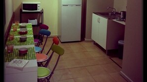A compact kitchen with a dining table set for four, a microwave, a refrigerator, and a sink. - City Drops Hostel (Porto)
