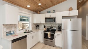 A modern kitchen with white cabinets, stainless steel appliances, a wooden ceiling, and a window.