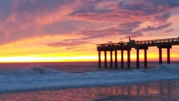 A pier extending into the ocean with a sunset in the background.