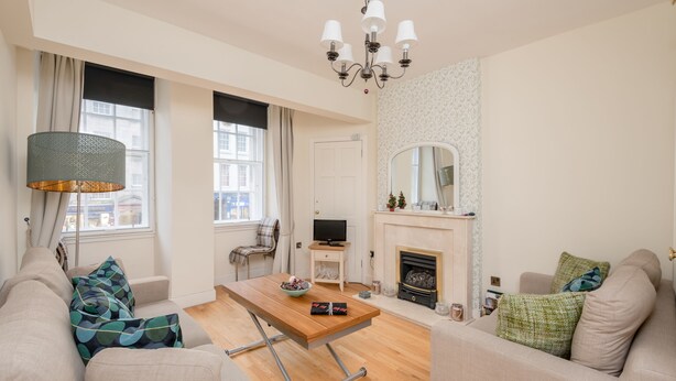 A living room with a sofa, a coffee table, a TV, a fireplace, and a lamp. - Silver Lining - Luxury Jackson Apartment (Edinburgh)