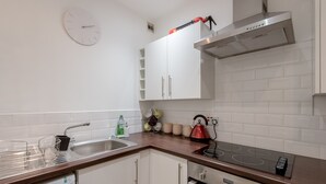 A modern kitchen with white cabinets, a stainless steel sink, a red kettle, and a built-in oven. - Silver Lining - Luxury Jackson Apartment (Edinburgh)