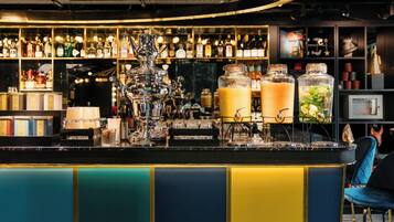 Uma área de bar com diversos frascos e copos, um grande jarro decorativo e um balcão com design colorido.