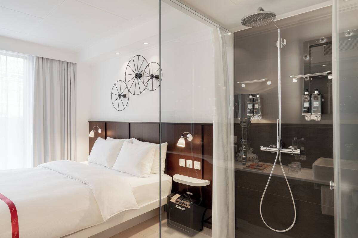 Ein modernes Hotelzimmer mit einem großen Bett, einer in Glas eingefassten Dusche und einem minimalistischen Design.
