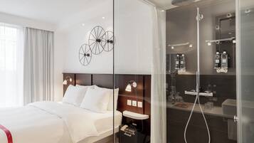 A modern hotel room with a large bed, a glass-enclosed shower, and a minimalist design.