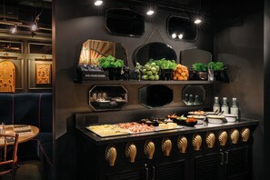 A buffet setup with various food items and a seating area with a table and chairs. - Ruby Lucy Hotel London by IHG (London)
