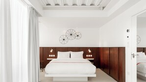 A modern bedroom with a central bed, wooden headboard, and a decorative wall piece. - Ruby Lucy Hotel London by IHG (London)