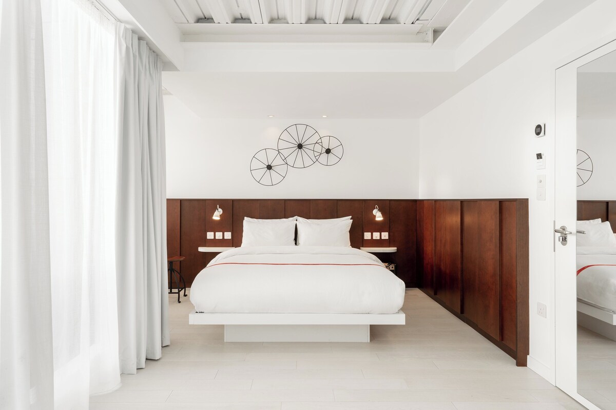 A modern bedroom with a central bed, wooden headboard, and a decorative wall piece.