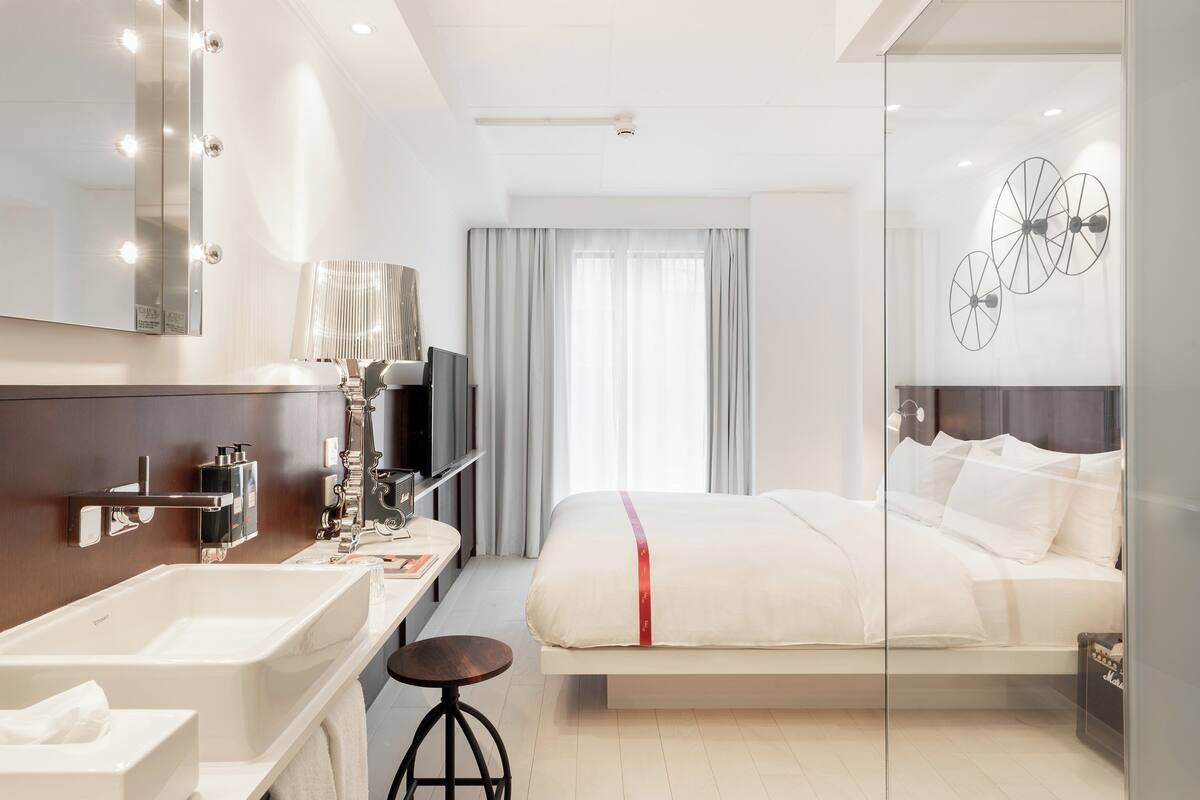 Ein modernes Hotelzimmer mit einem großen Bett, einem Schminktisch mit Spiegel und einem Fernseher.