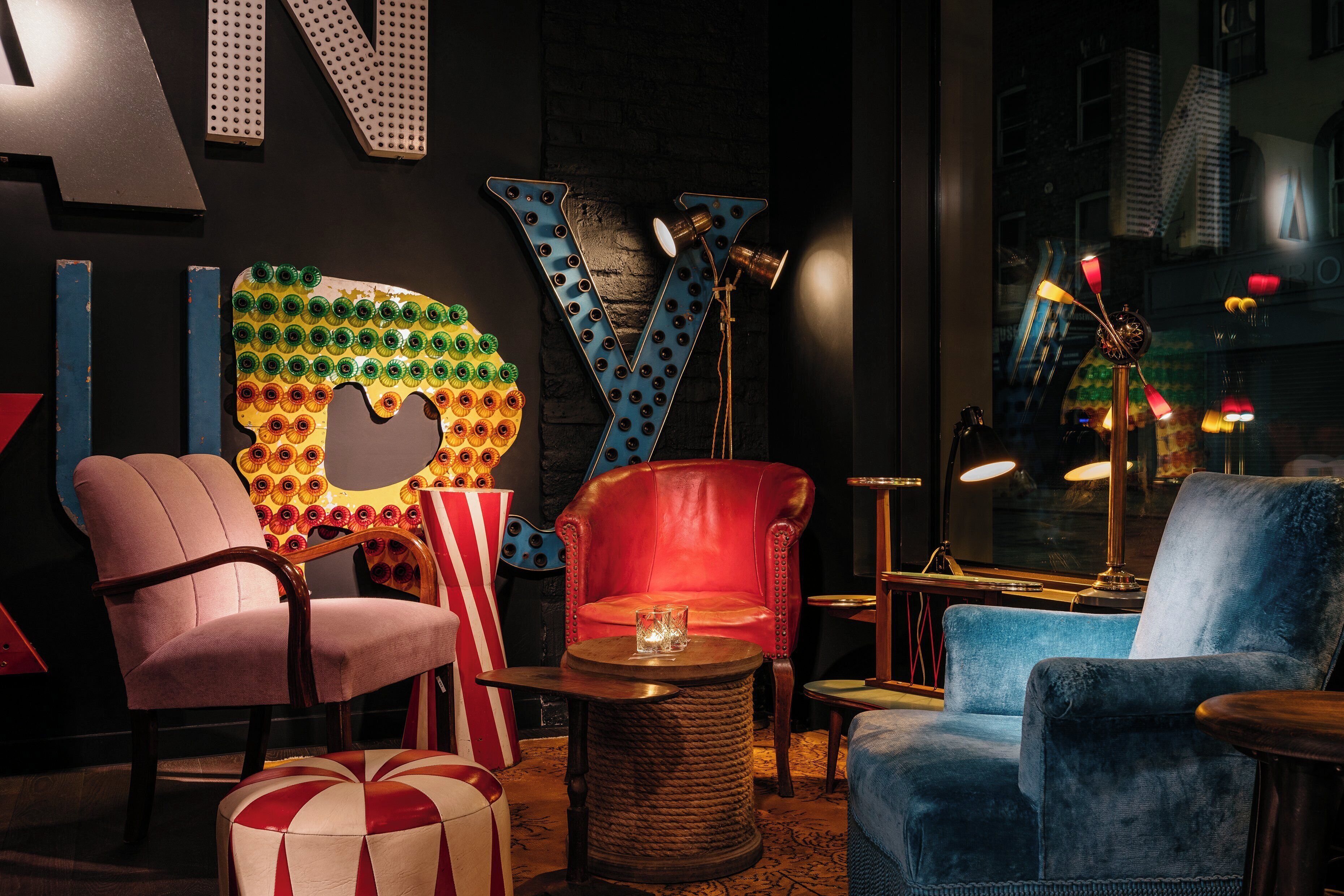 A cozy lounge area with a large, colorful letter 'V' decoration, plush seating, and a small round table with a glass.