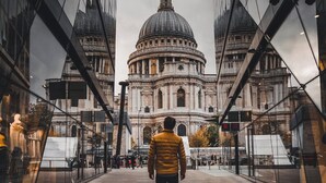 A person walking towards a historic building with a dome, flanked by modern glass structures.