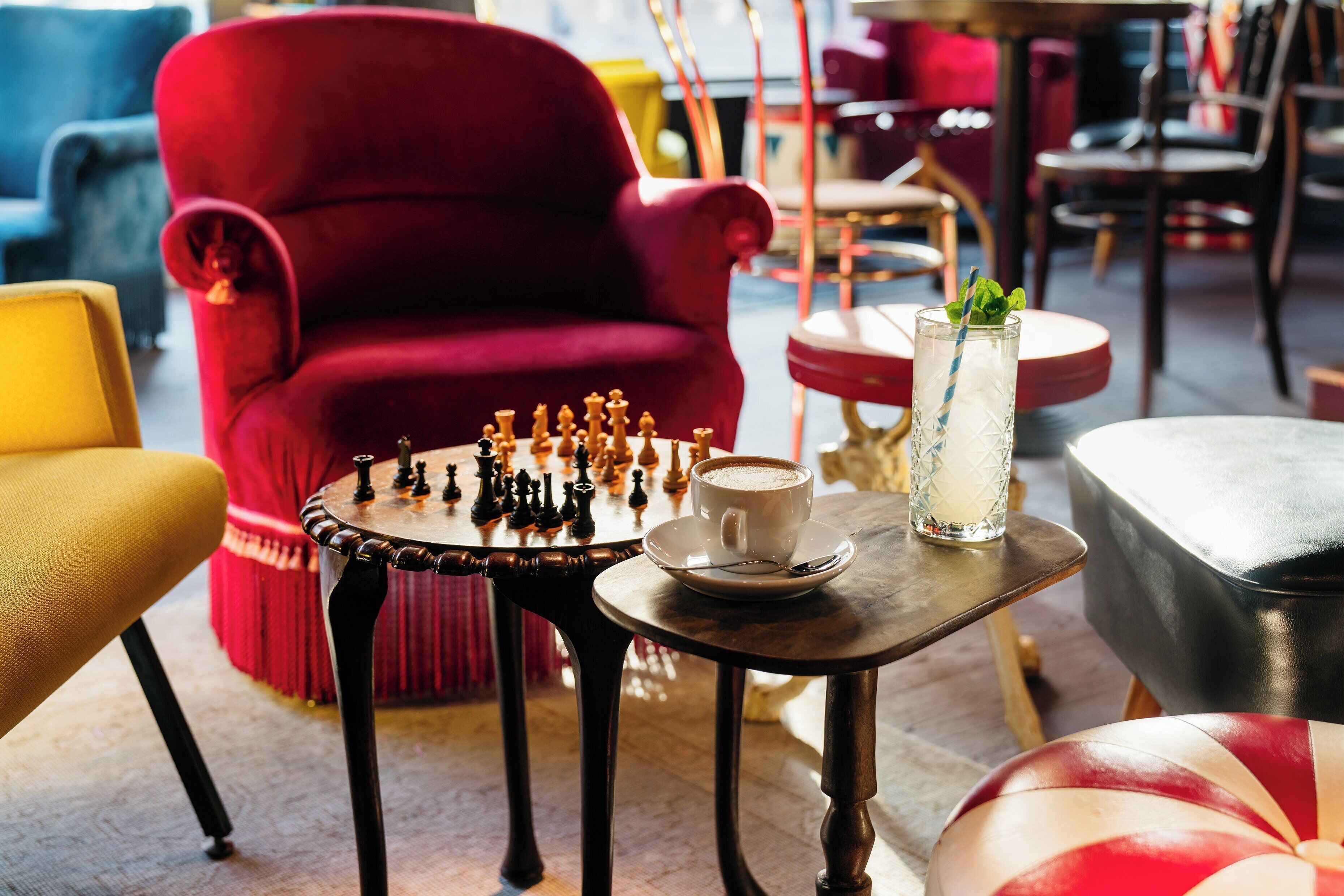 A cozy seating area with a red armchair, a chessboard, a cup of coffee, and a glass of water on a small table.