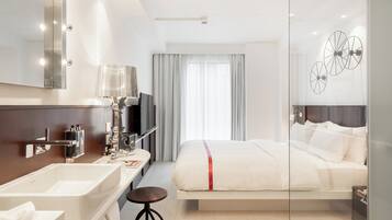 A modern hotel room with a large bed, a vanity with a mirror, and a television.